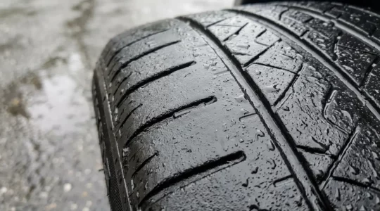 Gros plan sur un pneu automobile usé avec témoins d'usure visibles sur route mouillée